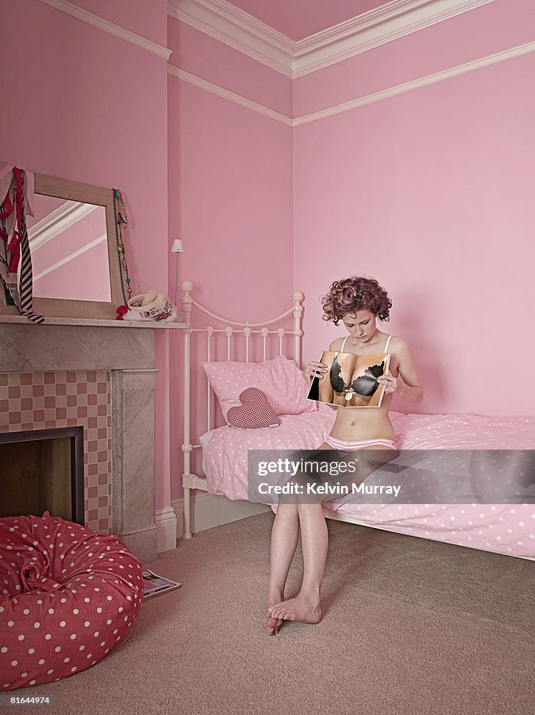 Woman in pink room, holding up magazine to body.