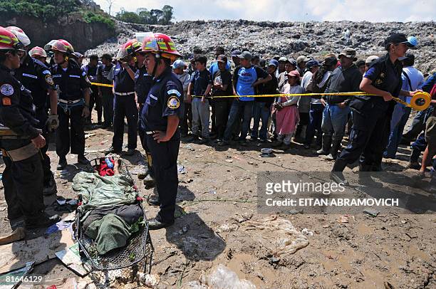 Firefighters wait to carry the body of a man killed by a mudslide at a garbage dump in Guatemala City on June 20, 2008. At least seven people died...
