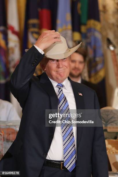 President Donald Trump puts on a Stetson cowboy hat while touring a Made in America product showcase in the East Room of the White House July 17,...