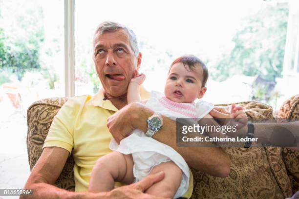 youthful grandpa making a silly face while holding granddaughter. - man tongue stock pictures, royalty-free photos & images