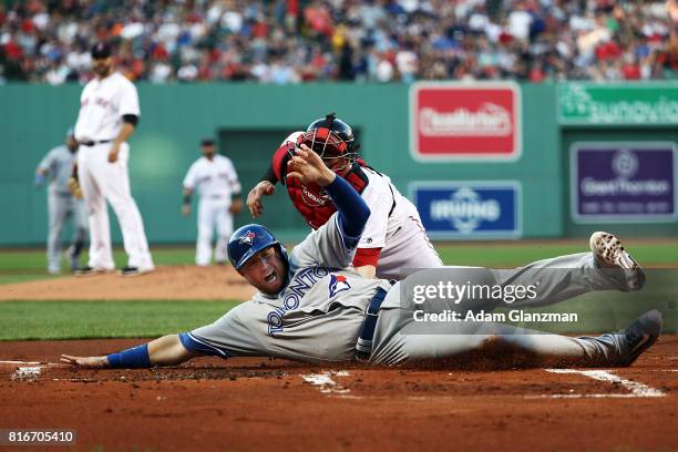 Justin Smoak of the Toronto Blue Jays slides safely under the tag of Christian Vazquez of the Boston Red Sox in the first inning of a game at Fenway...