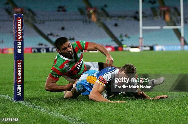 Jordan Atkins of the Titans scores a try despite the tackle of Nathan Merritt of the Rabbitohs tackles during the round 15 NRL match between the...