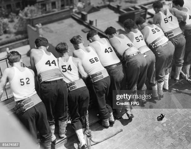 Trainee firemen watch their colleagues descend by rope from the roof of a building at a training centre in New York, circa 1950.