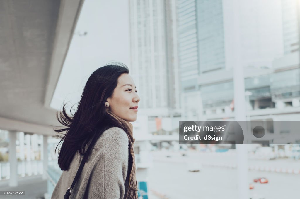 Beautiful young Asian lady overlooking cityscape of Hong Kong on urban bridge