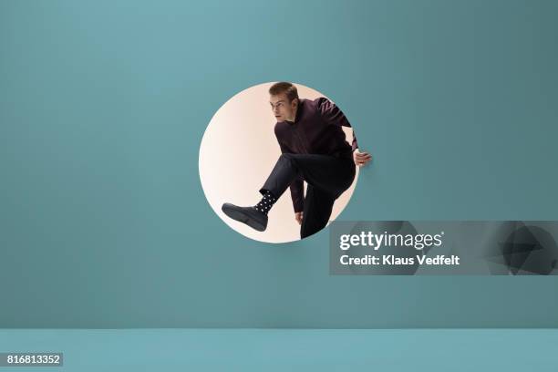 man stepping threw round opening in coloured wall - emergere foto e immagini stock