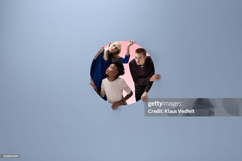 Three people crawling out of round opening in coloured wall