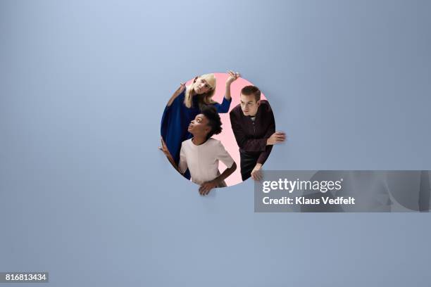 three people crawling out of round opening in coloured wall - round three bildbanksfoton och bilder