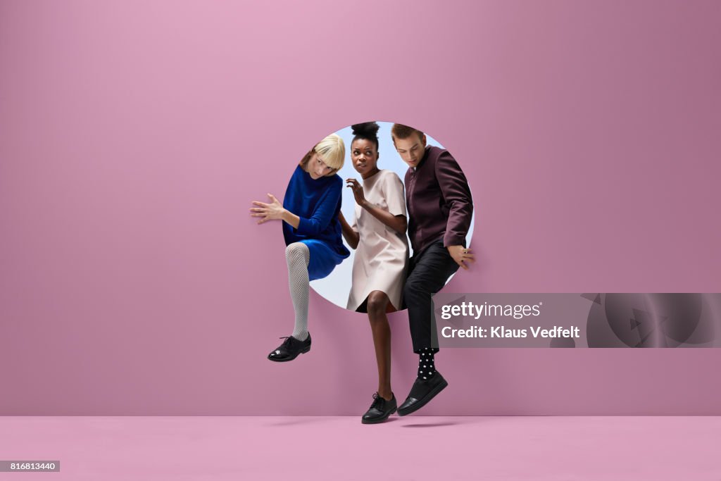 Three people crawling out of round opening in coloured wall
