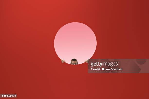 man peeking out of round opening in coloured wall - regarder à la dérobée photos et images de collection