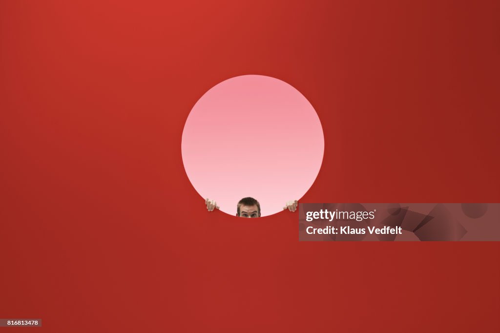 Man peeking out of round opening in coloured wall