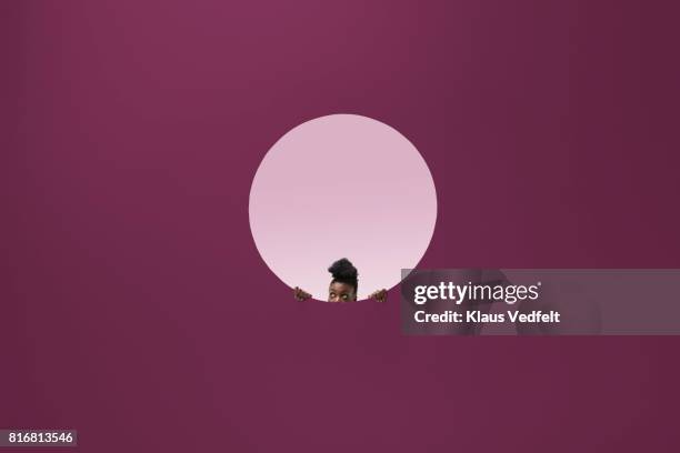 woman peeking out of round opening in coloured wall - breakthrough concept stock-fotos und bilder