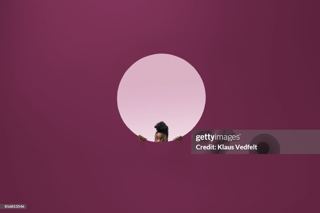 Woman peeking out of round opening in coloured wall
