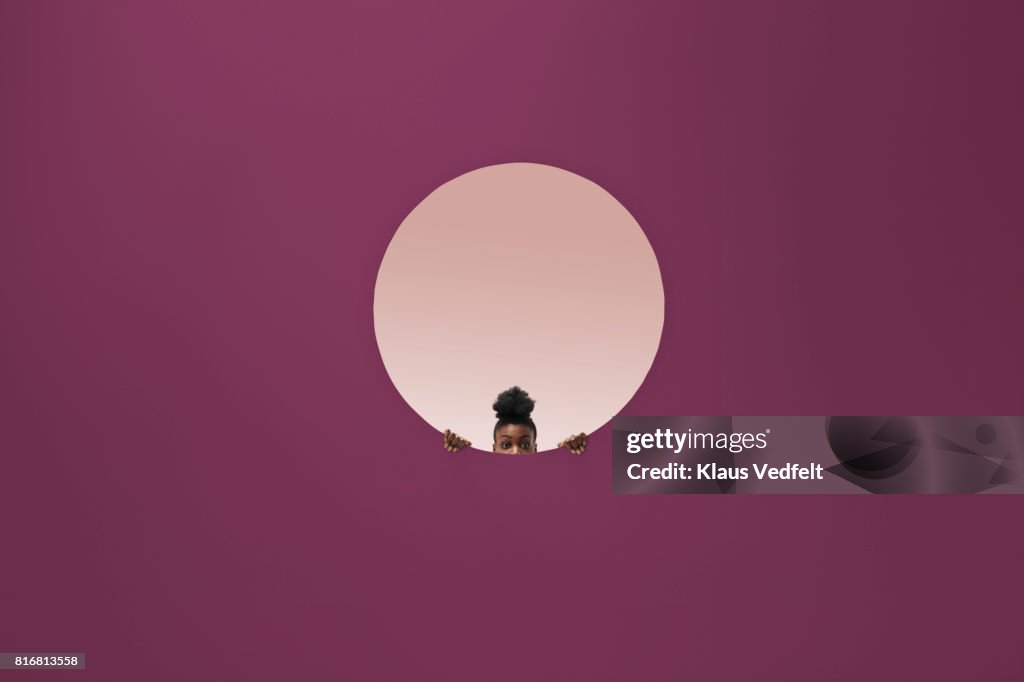 Woman peeking out of round opening in coloured wall