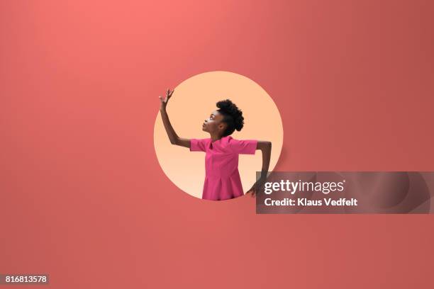 woman placed inside round opening in coloured wall - pink dress stockfoto's en -beelden