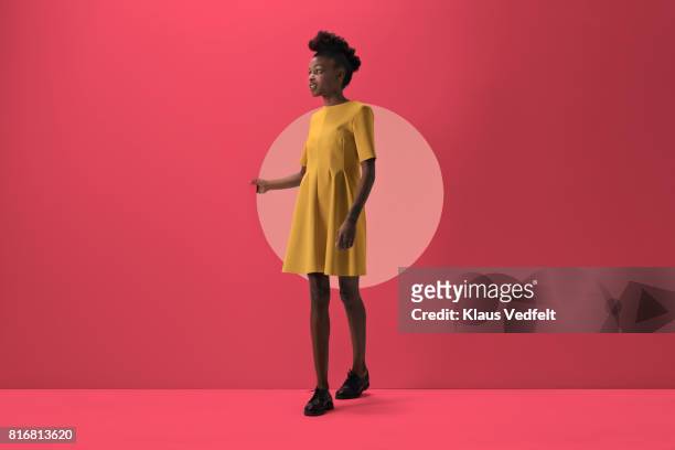 woman walking out from woman peeking out of round opening in coloured wall - jurk stockfoto's en -beelden