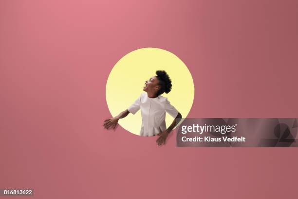 woman laughing, placed inside round opening in coloured wall - creatividad fotografías e imágenes de stock