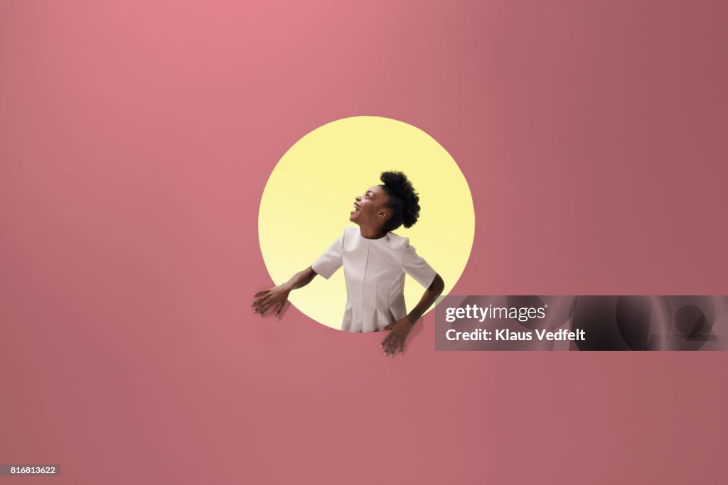 Woman laughing, placed inside round opening in coloured wall