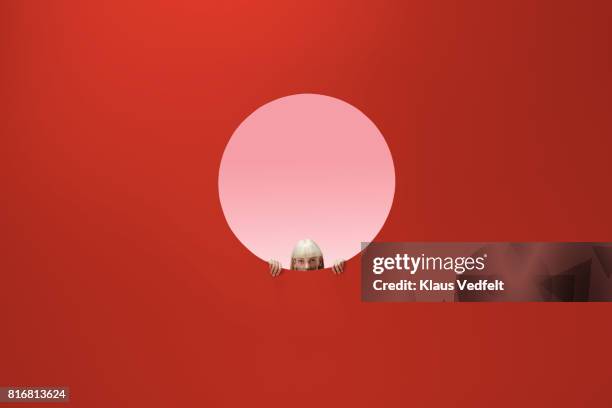 woman peeking out of round opening in coloured wall - appearance stock-fotos und bilder