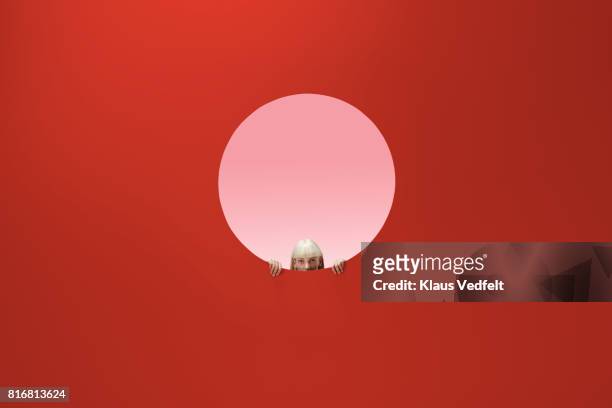 woman peeking out of round opening in coloured wall - appearance photos et images de collection