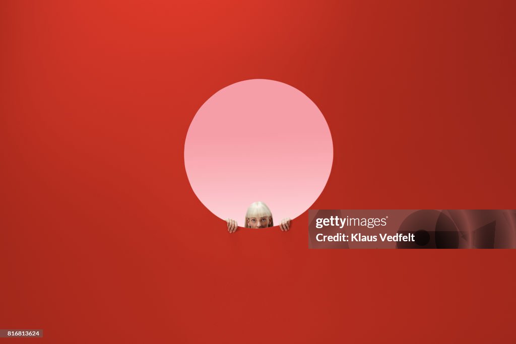 Woman peeking out of round opening in coloured wall