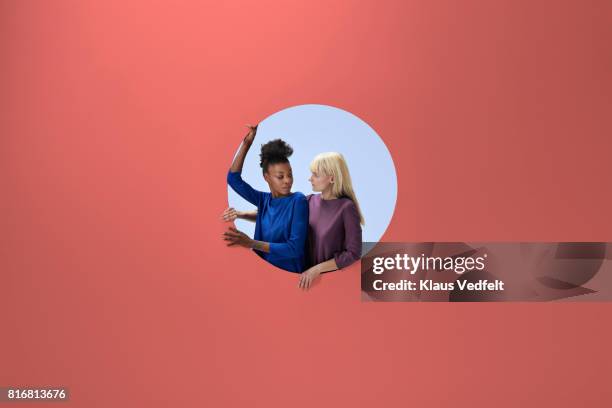 two women sitting inside round opening in coloured wall - changing appearance photos et images de collection