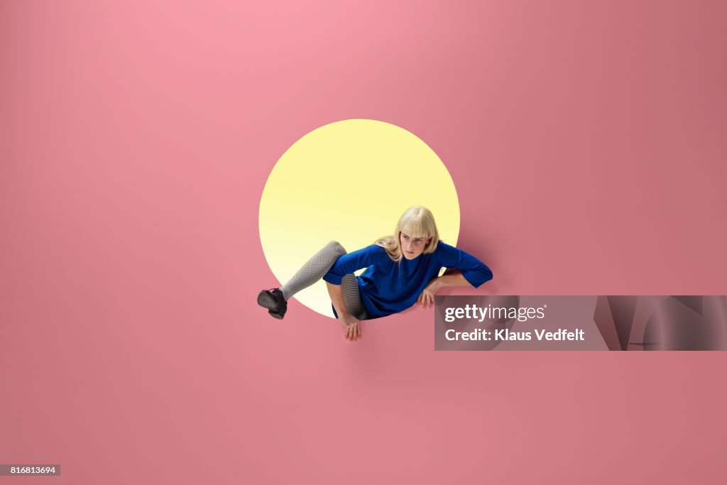 Woman crawling out of round opening in coloured wall