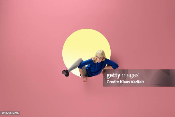 woman crawling out of round opening in coloured wall - climbers stockfoto's en -beelden