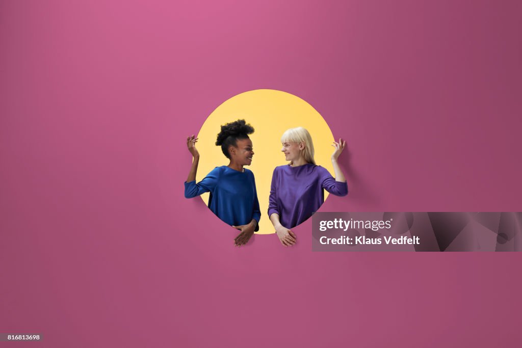 Two women smiling, sitting inside round opening in coloured wall