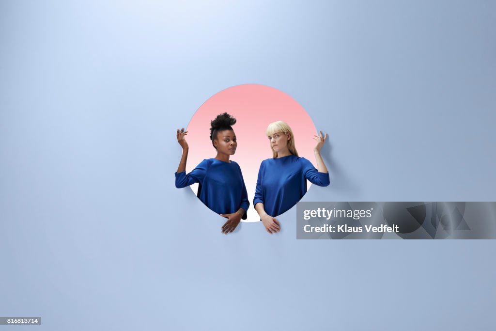 Two women sitting inside round opening in coloured wall