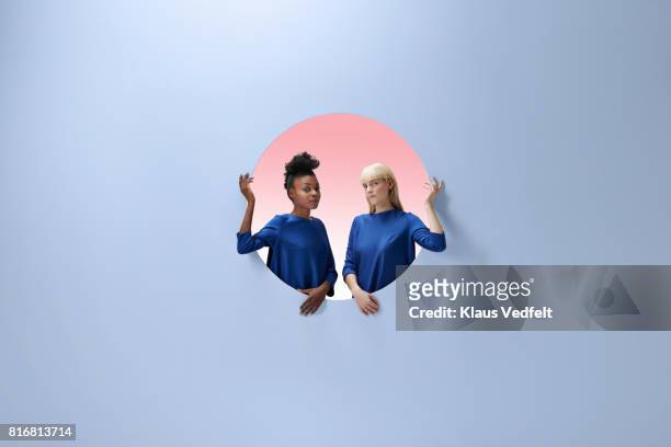 Two women sitting inside round opening in coloured wall