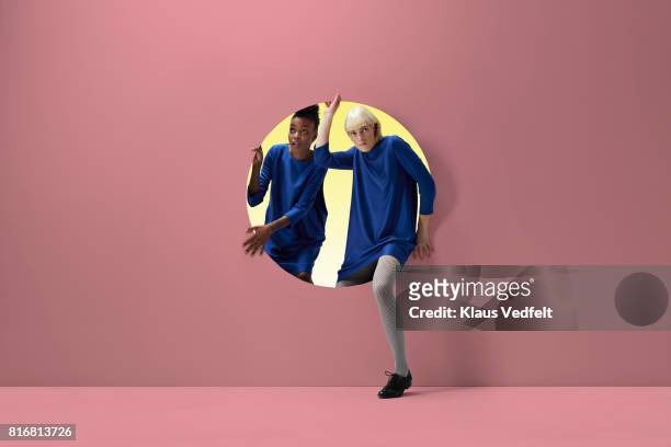 two women peeking out of round opening in coloured wall - spähen stock-fotos und bilder