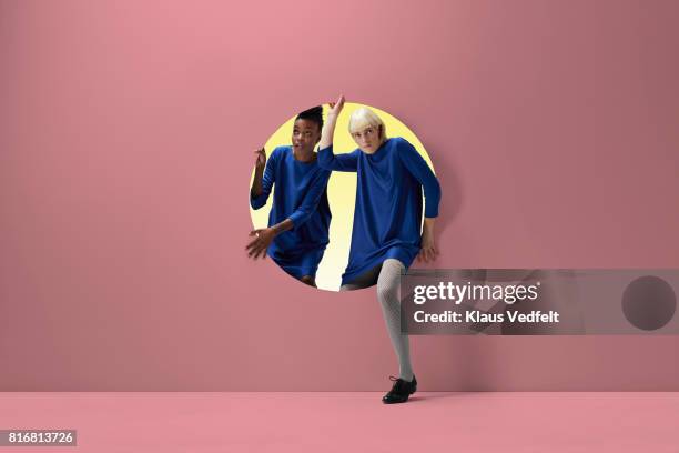 two women peeking out of round opening in coloured wall - regarder à la dérobée photos et images de collection