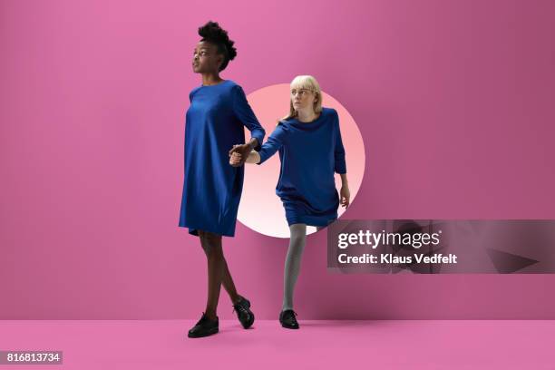 two women peeking out of round opening in coloured wall - couple studio stockfoto's en -beelden