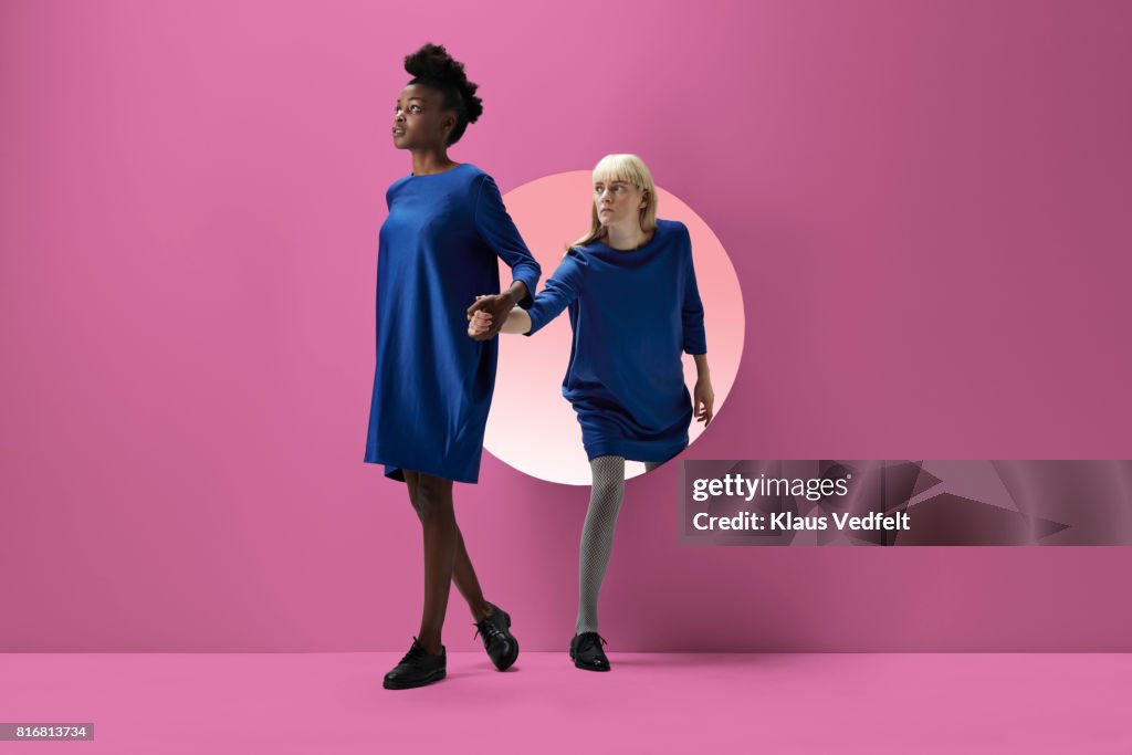 Two women peeking out of round opening in coloured wall