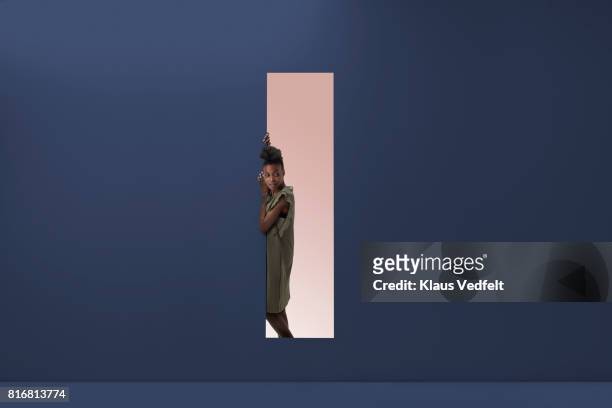 woman standing in rectangular opening of coloured wall - spähen stock-fotos und bilder