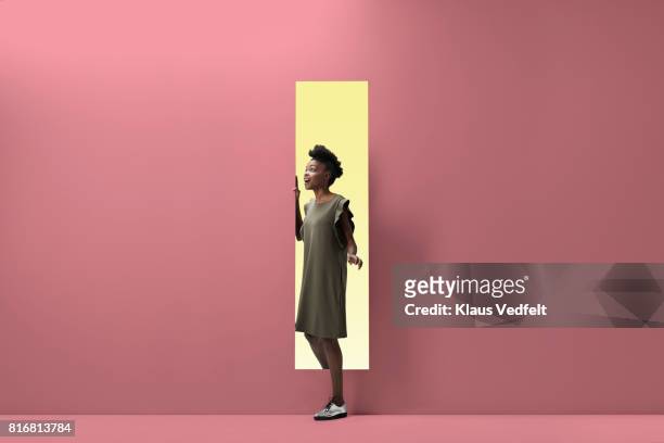 woman walking out of rectangular opening of coloured wall - verrassing stockfoto's en -beelden