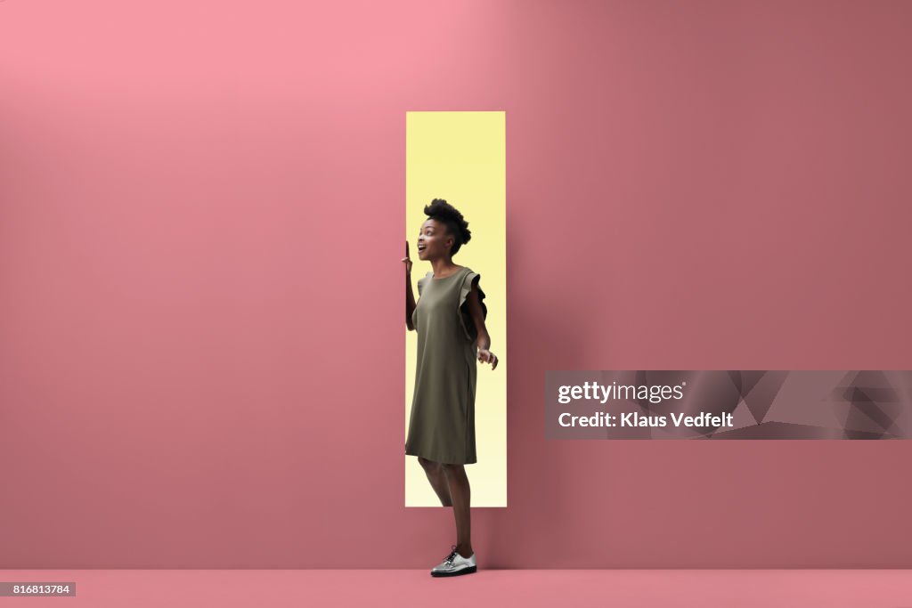 Woman walking out of rectangular opening of coloured wall