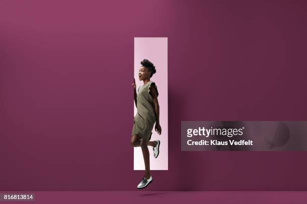 woman jumping out of rectangular opening of coloured wall - leap forward stock pictures, royalty-free photos & images