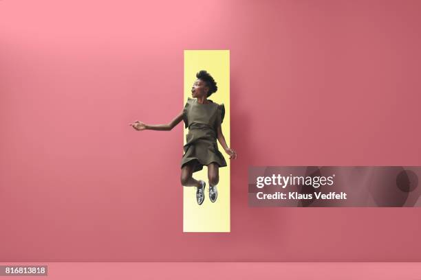 woman jumping out of rectangular opening of coloured wall - people jumping stock-fotos und bilder