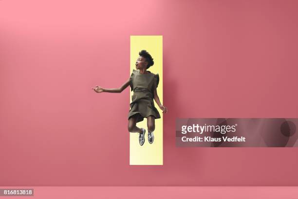 woman jumping out of rectangular opening of coloured wall - saltare foto e immagini stock