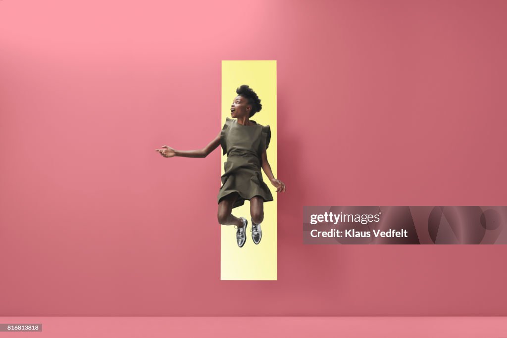 Woman jumping out of rectangular opening of coloured wall