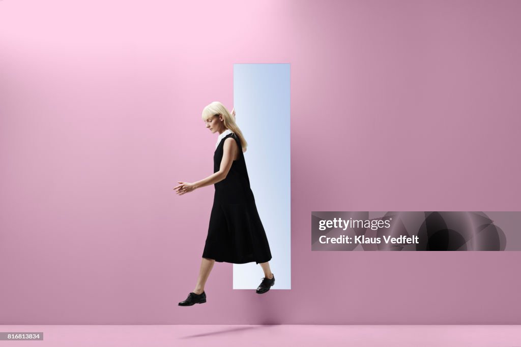 Woman stepping threw rectangular opening of coloured wall