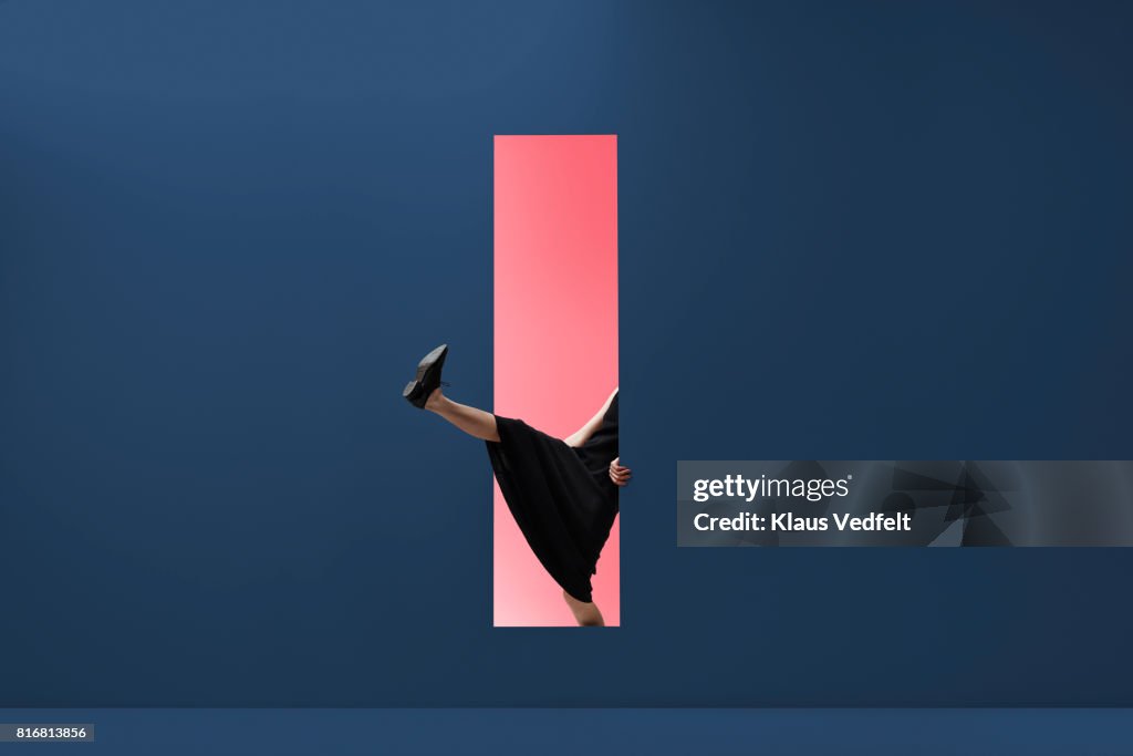 Woman stepping threw rectangular opening of coloured wall