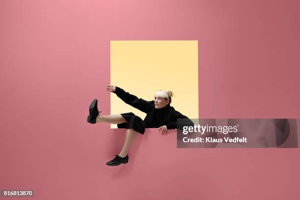 Woman hanging on to square opening in coloured wall, feet dangling