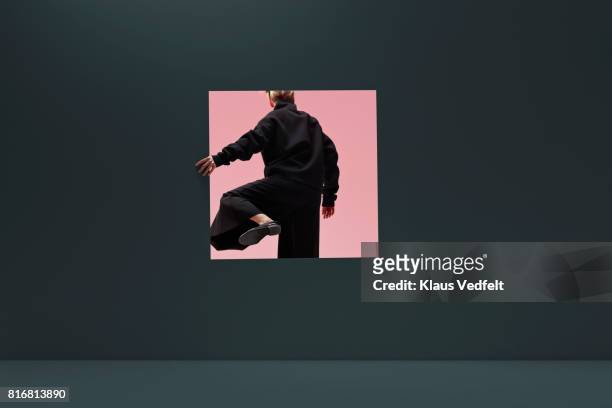 woman stepping threw square opening in coloured wall - neugierde stock-fotos und bilder