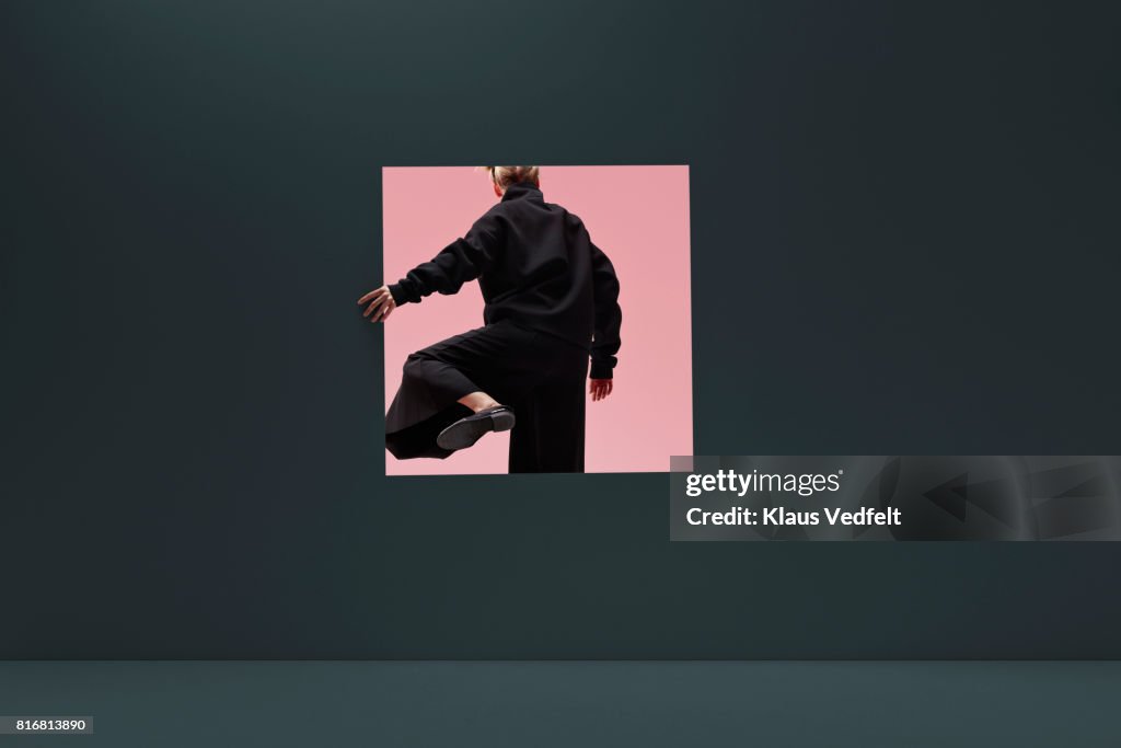 Woman stepping threw square opening in coloured wall