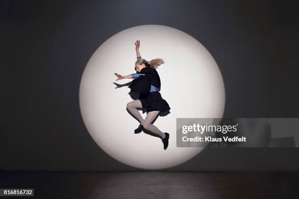 woman jumping in round theatre spotlight, in studio with concrete floor - spotlit stockfoto's en -beelden