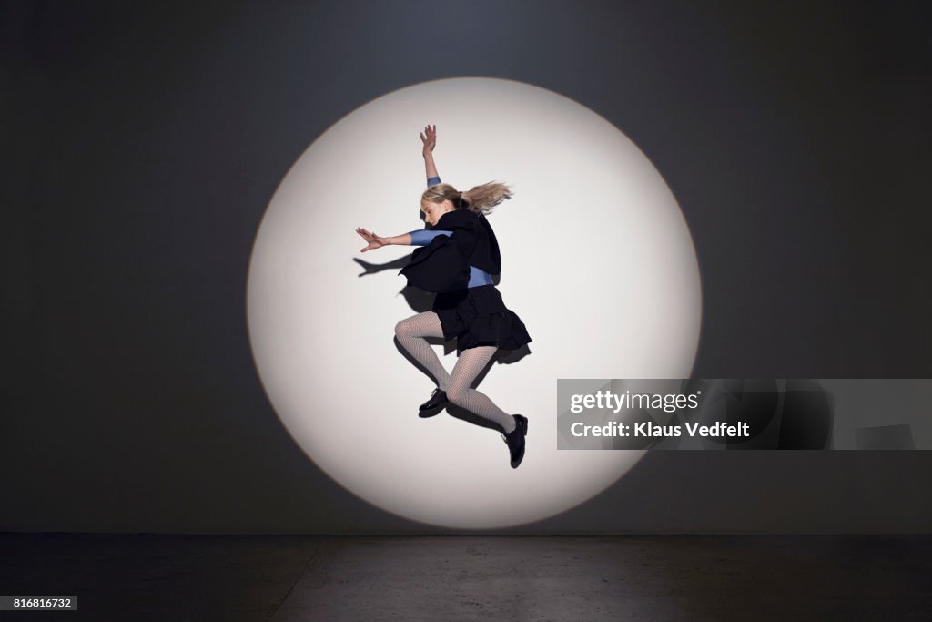 Woman jumping in round theatre spotlight, in studio with concrete floor