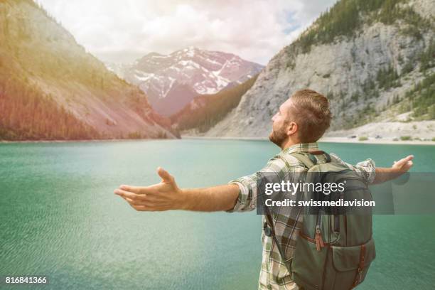 young man hiker arms outstretched at mountain lake - canmore stock pictures, royalty-free photos & images