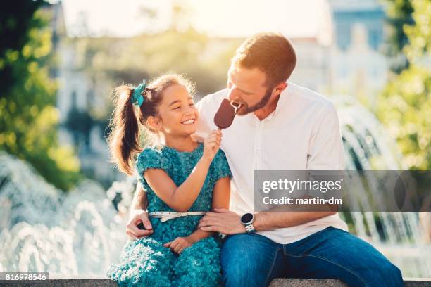 giovane padre e figlia che mangiano gelato alla fontana - giorno dei bambini foto e immagini stock